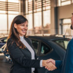 Cheerful car dealer handshake with customer in showroom.
